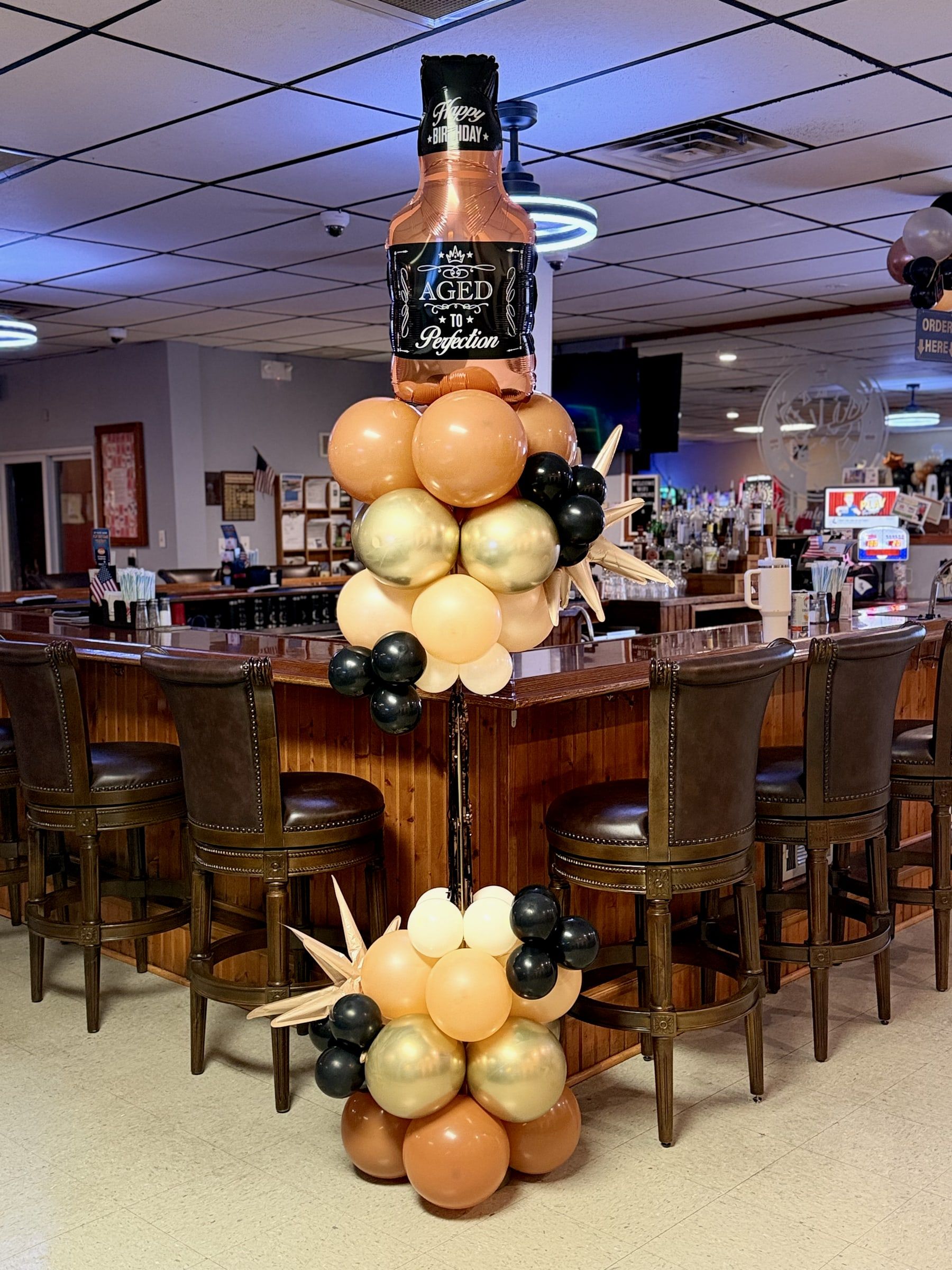A tall balloon sculpture shaped like a whiskey bottle, standing in a restaurant bar