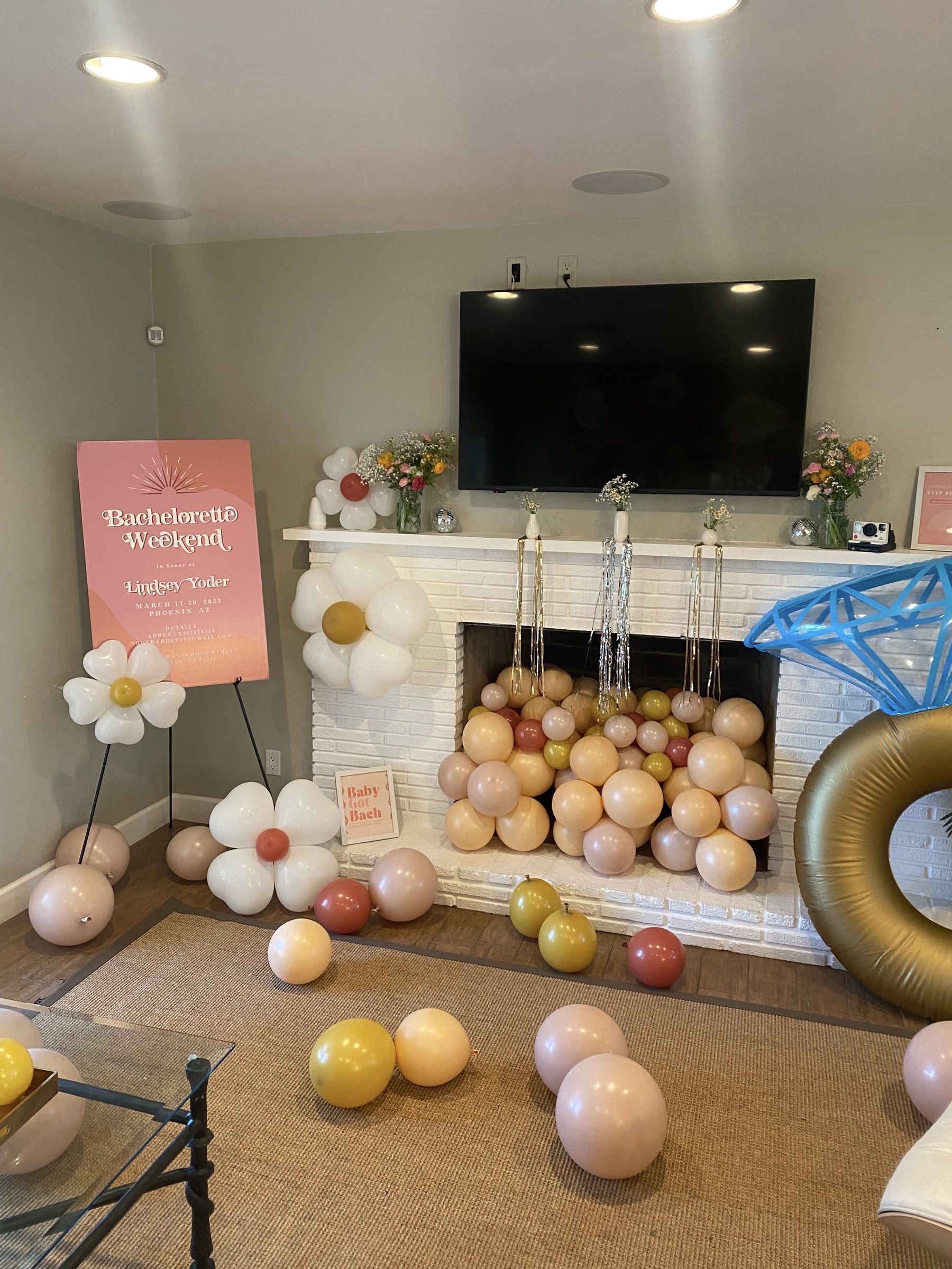 Peach, blush, gold and terracotta balloons spilling out of a white brick fireplace, with daisy balloons and a giant diamond ring balloon