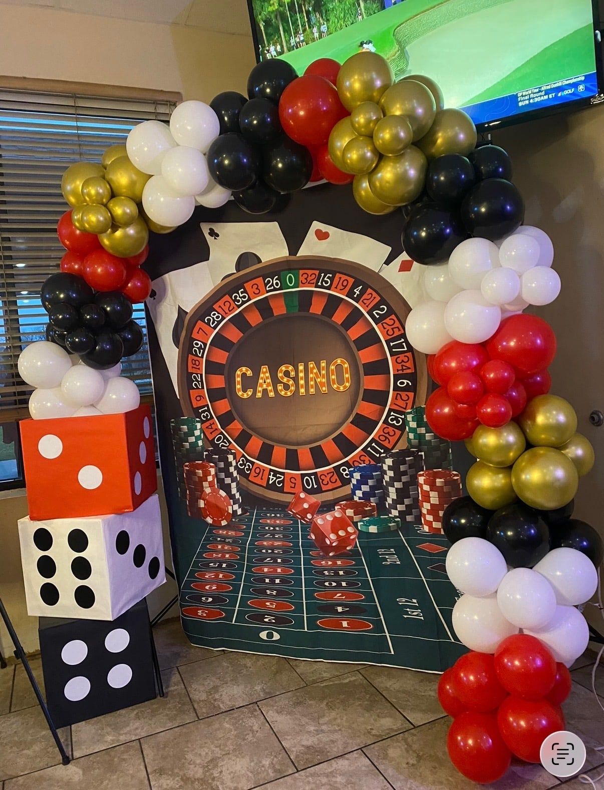 A red, black, white and gold balloon arch framing a casino backdrop with oversized dice