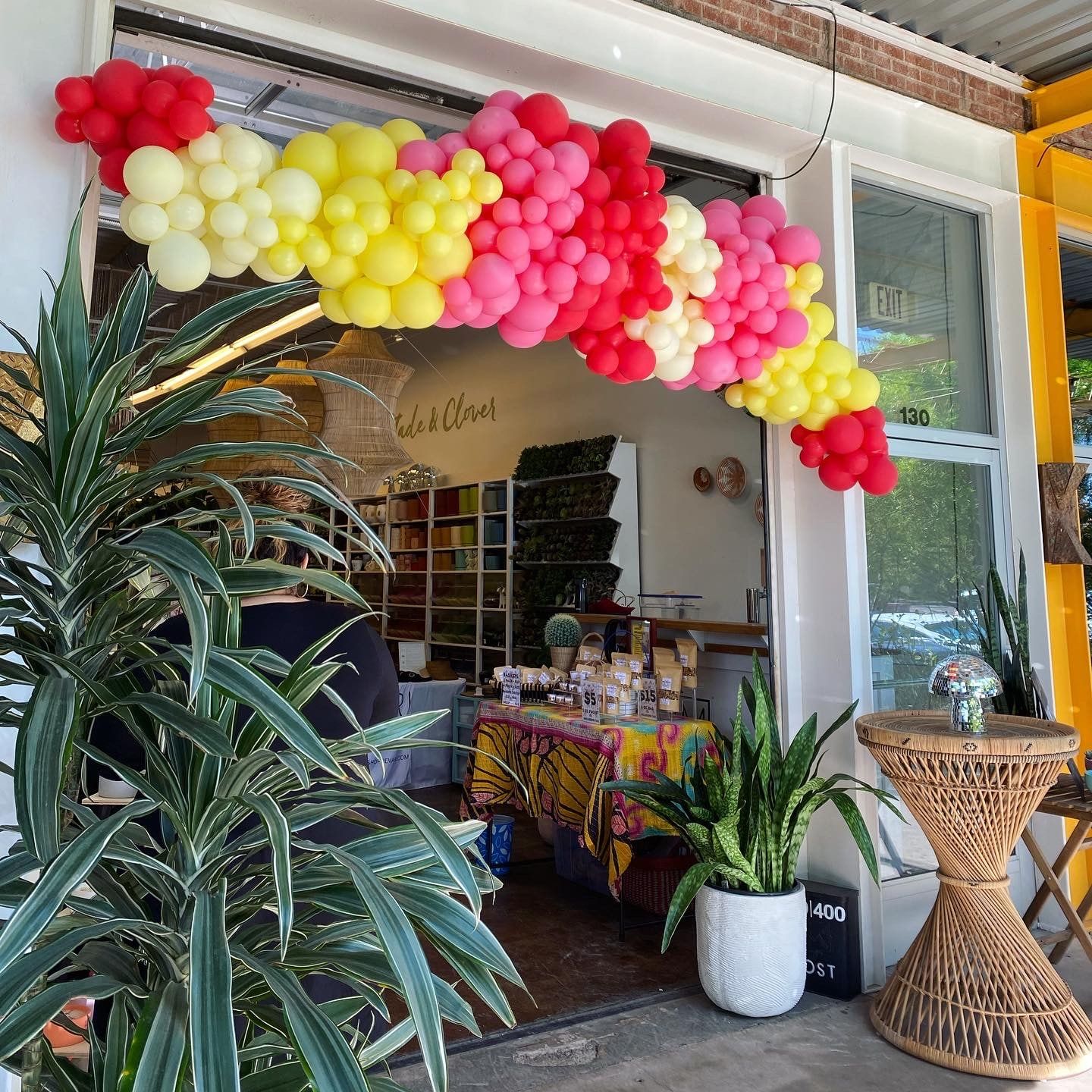 A bright red, yellow and pink balloon garland framing the open front of a shop