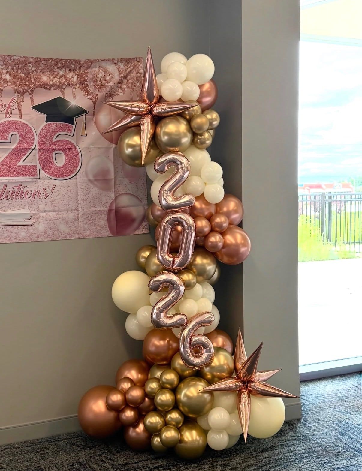 A column of chrome gold, rose gold and cream balloons with foil numbers spelling 2026 and foil stars