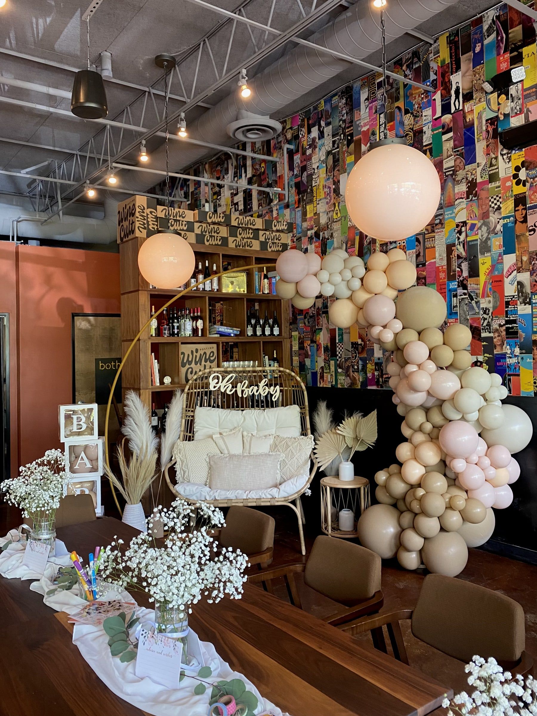A neutral organic balloon installation curving over a lounge setting at a baby shower inside a restaurant with a colorful book wall
