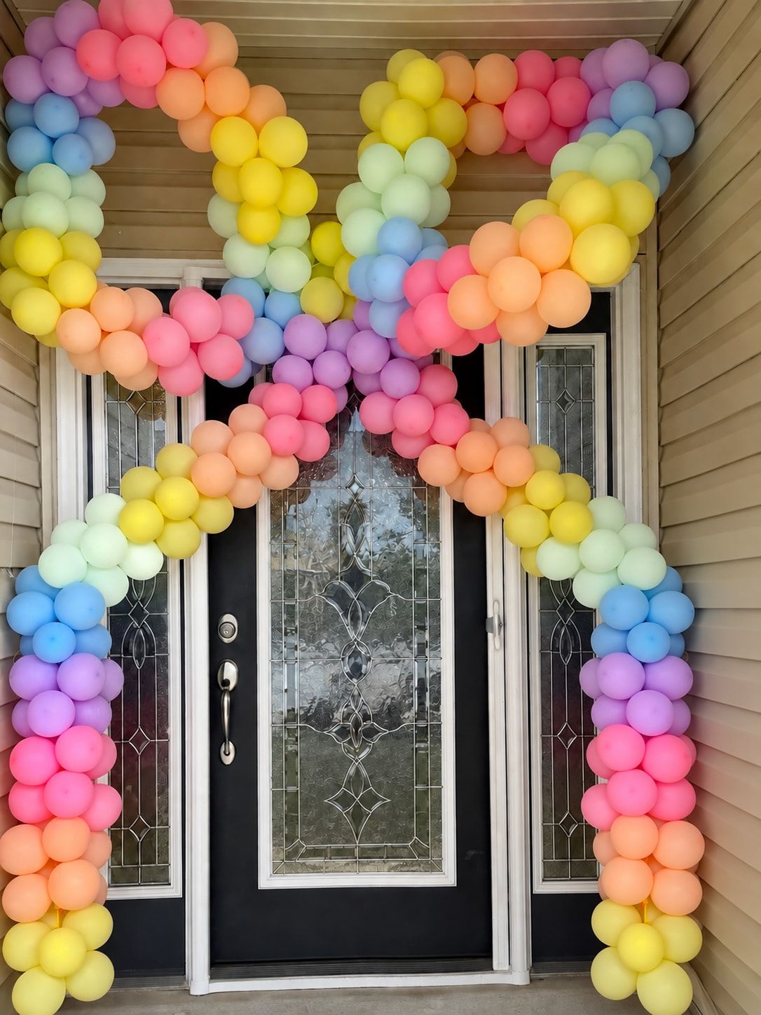 A pastel rainbow balloon garland framing a black front door, rising up both sides and zigzagging across the top