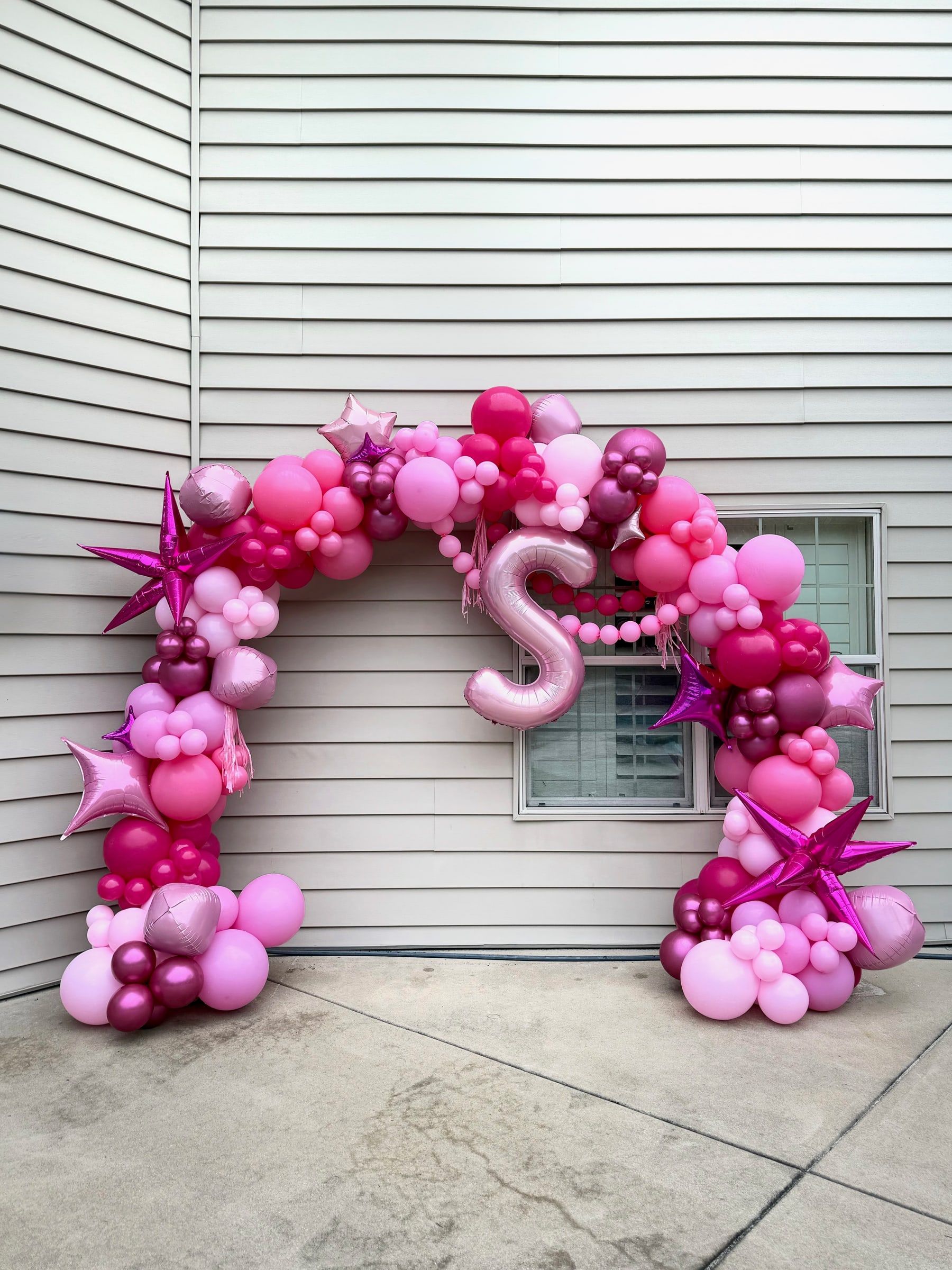 A large organic arch of pink balloons with star-shaped foil accents and a pink letter S