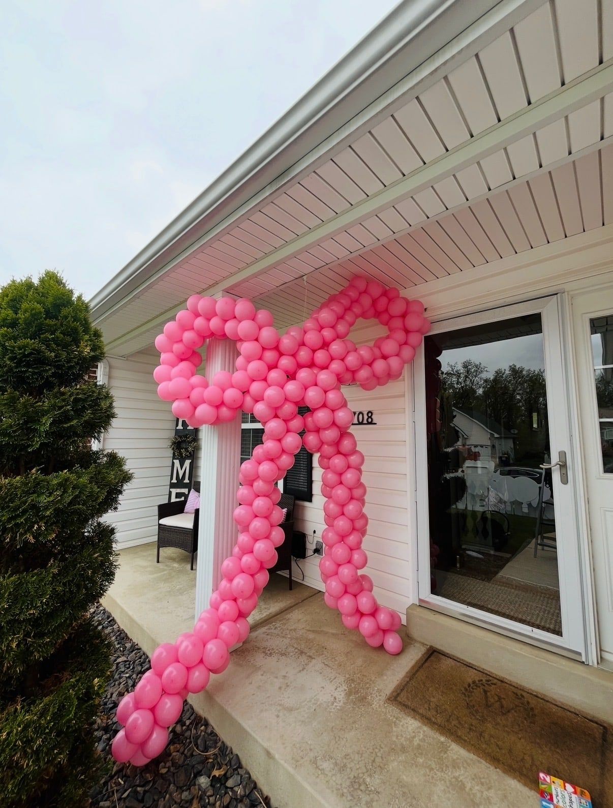 A giant pink bow made of balloons, mounted on the front of a house